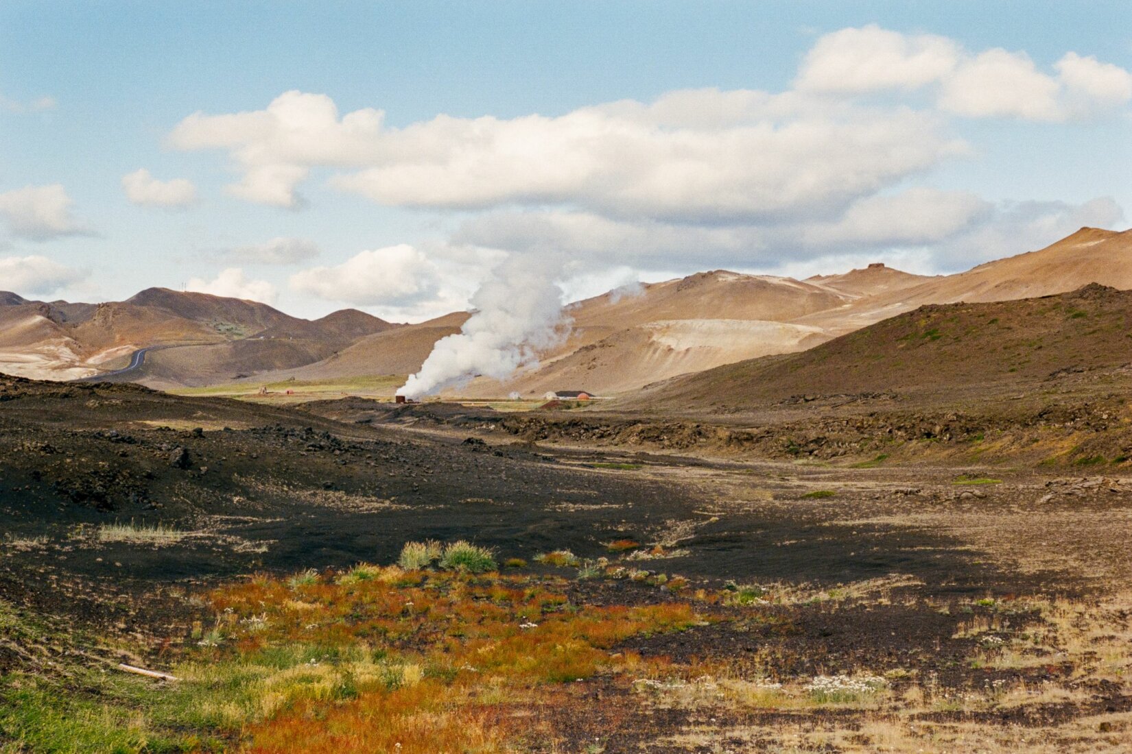 Foto: hügelige Landschaft mit gelber, brauner und schwarzer Erde, Dampf steigt in der Ferne auf